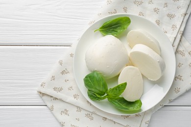 Photo of Pieces of delicious mozzarella cheese and basil on white wooden table, top view