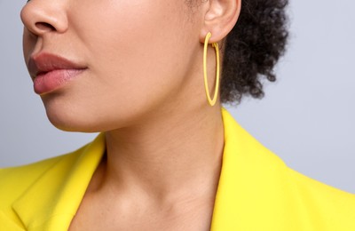 Photo of Young woman wearing elegant yellow earring on light grey background, closeup