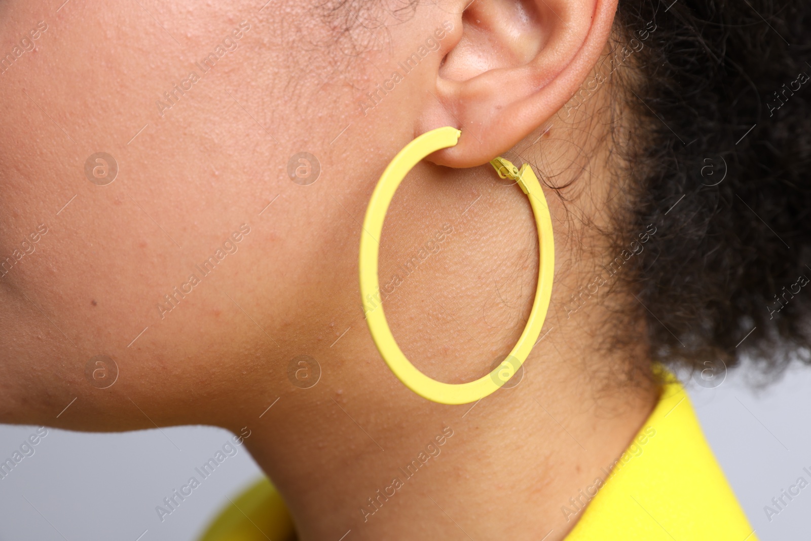 Photo of Young woman wearing elegant yellow earring on light grey background, closeup