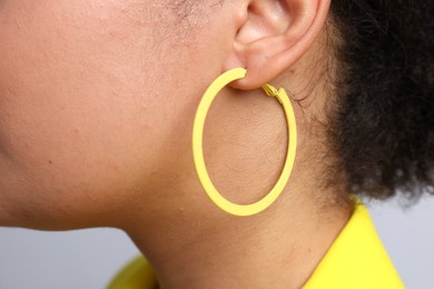 Photo of Young woman wearing elegant yellow earring on light grey background, closeup