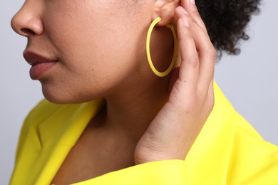 Photo of Young woman wearing elegant yellow earring on light grey background, closeup