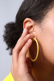 Photo of Young woman wearing elegant yellow earring on light grey background, closeup
