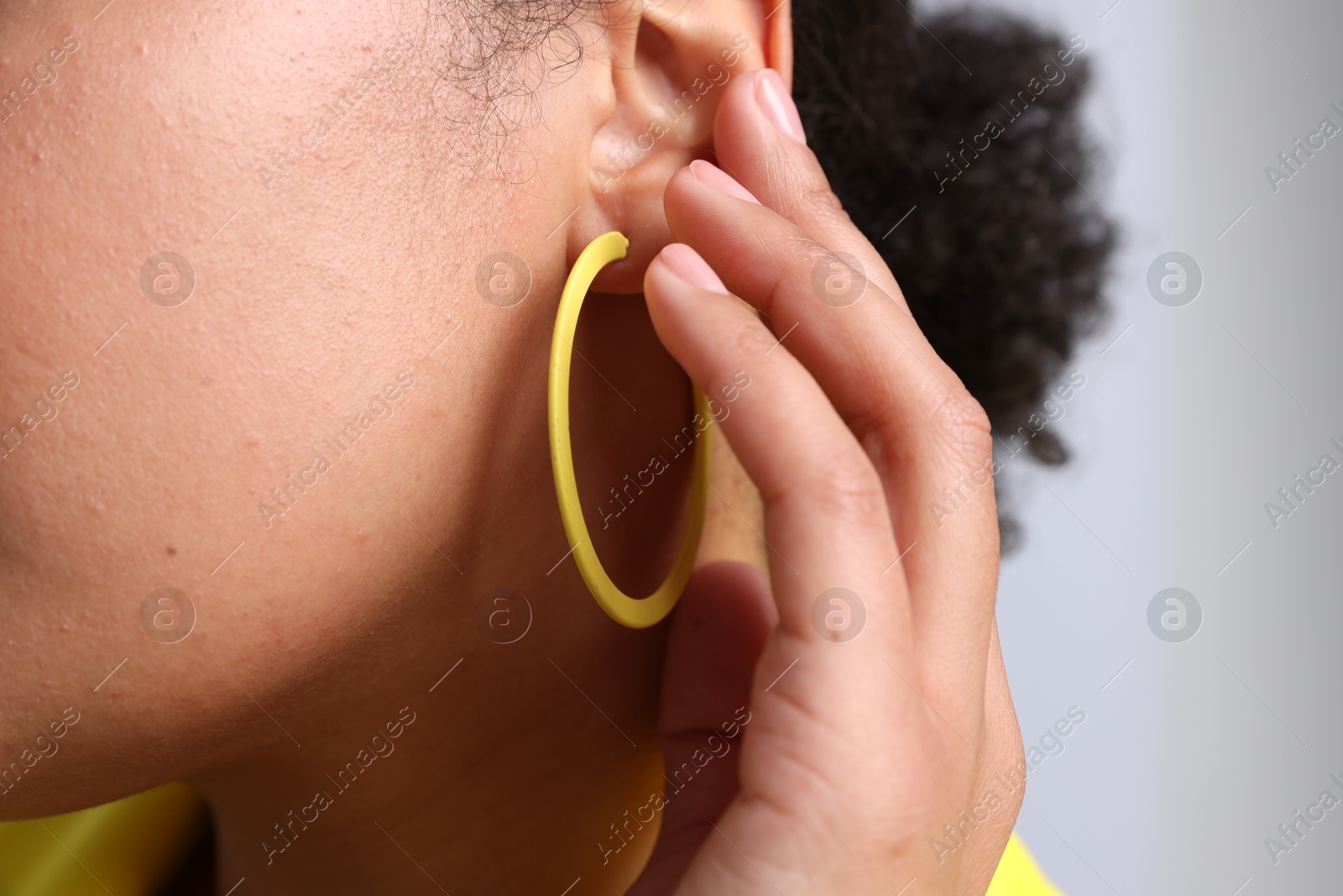 Young woman wearing elegant yellow earring on light grey background, closeup Photo of Young woman wearing elegant yellow earring on light grey background, closeup