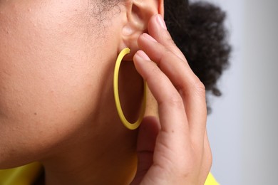 Photo of Young woman wearing elegant yellow earring on light grey background, closeup