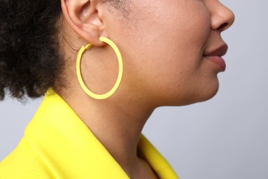 Photo of Young woman wearing elegant yellow earring on light grey background, closeup