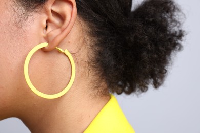 Photo of Young woman wearing elegant yellow earring on light grey background, closeup