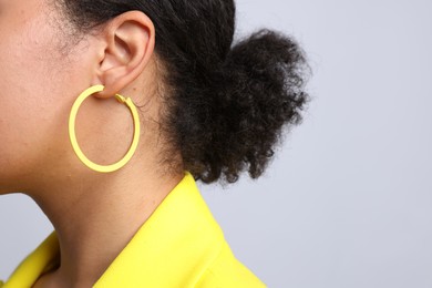 Photo of Young woman wearing elegant yellow earring on light grey background, closeup. Space for text