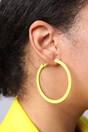 Photo of Young woman wearing elegant yellow earring on light grey background, closeup