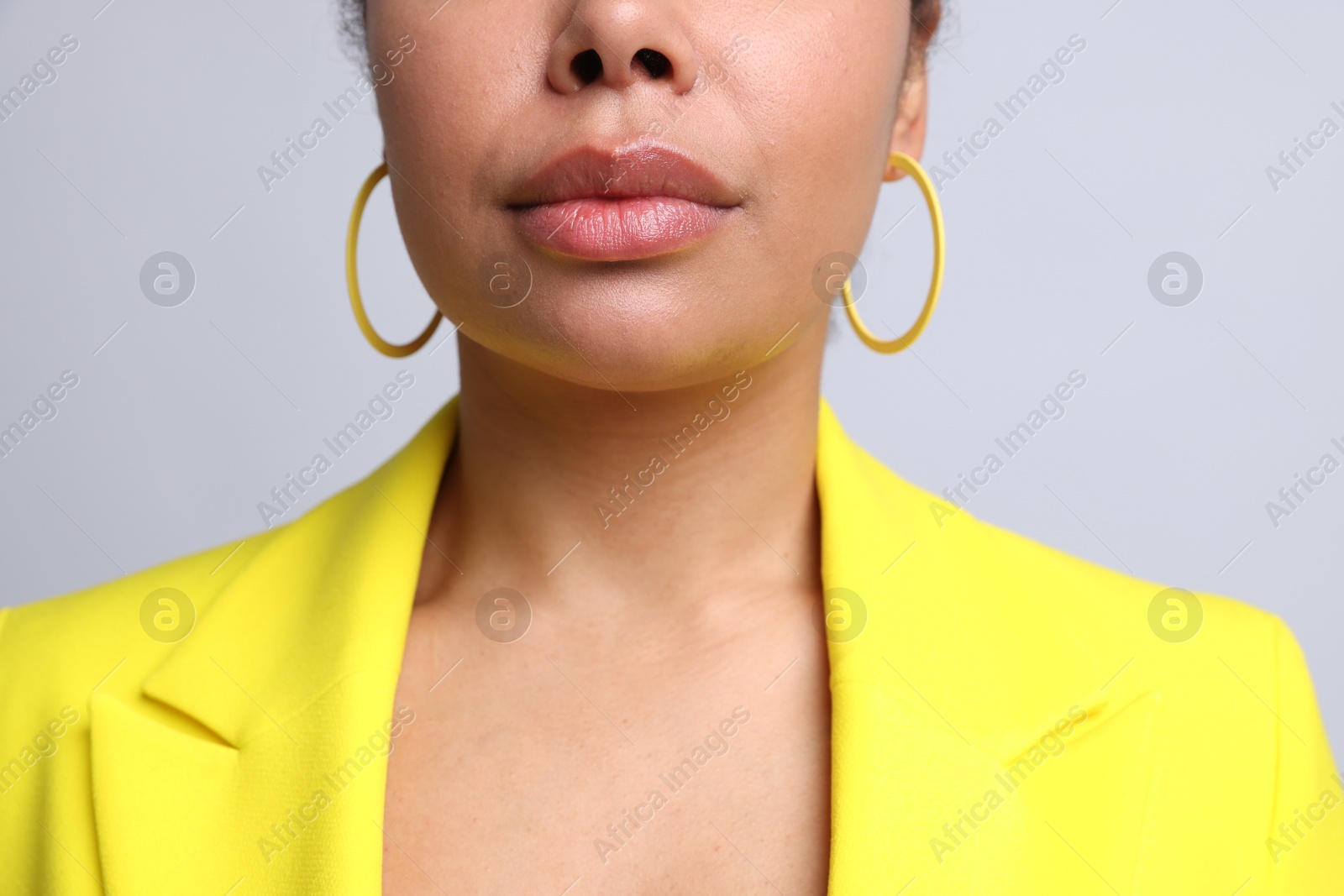Photo of Young woman wearing elegant yellow earrings on light grey background, closeup