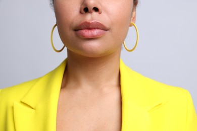 Photo of Young woman wearing elegant yellow earrings on light grey background, closeup
