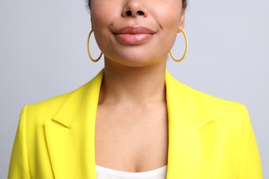 Photo of Young woman wearing elegant yellow earrings on light grey background, closeup