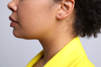 Photo of Young woman with pierced ear on light grey background, closeup
