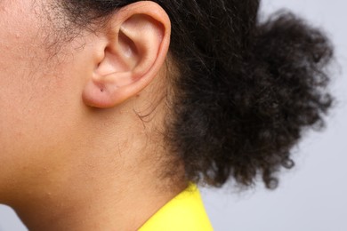 Photo of Young woman with pierced ear on light grey background, closeup