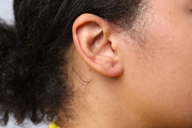 Photo of Young woman with pierced ear on light grey background, closeup
