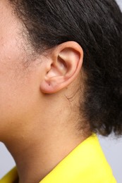 Photo of Young woman with pierced ear on light grey background, closeup