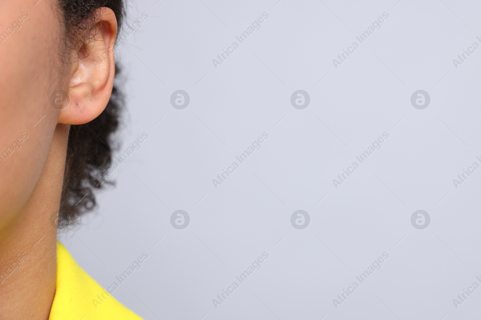 Young woman with pierced ear on light grey background, closeup. Space for text Photo of Young woman with pierced ear on light grey background, closeup. Space for text