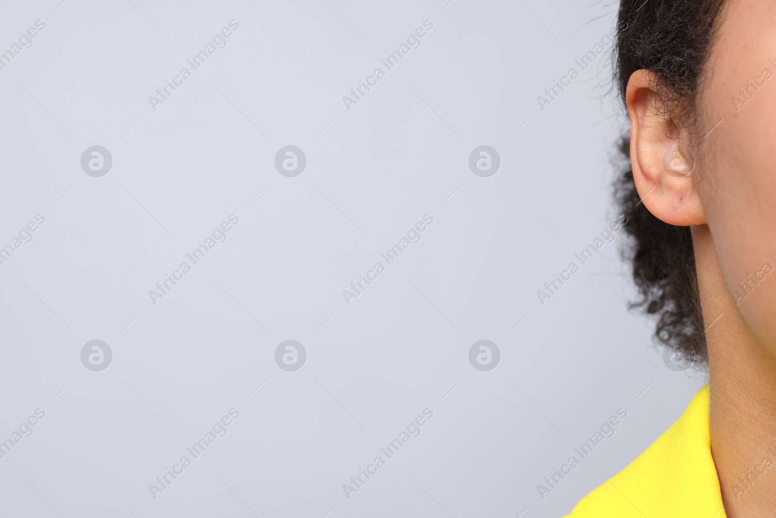 Young woman with pierced ear on light grey background, closeup. Space for text Photo of Young woman with pierced ear on light grey background, closeup. Space for text