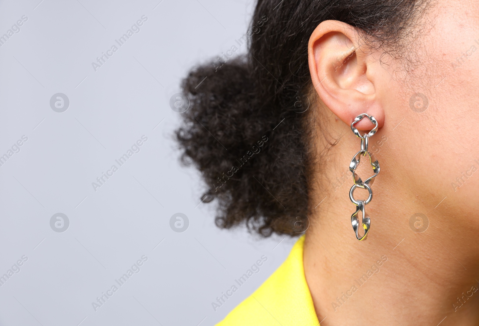 Photo of Young woman wearing elegant silver earring on light grey background, closeup. Space for text