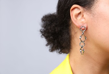 Photo of Young woman wearing elegant silver earring on light grey background, closeup. Space for text