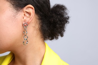 Photo of Young woman wearing elegant silver earring on light grey background, closeup. Space for text