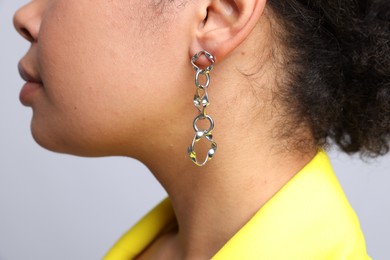 Photo of Young woman wearing elegant silver earring on light grey background, closeup