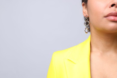 Photo of Young woman wearing elegant silver earring on light grey background, closeup. Space for text