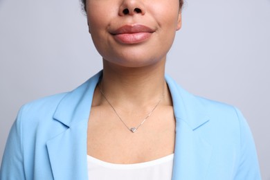 Photo of Young woman wearing elegant silver necklace on light grey background, closeup