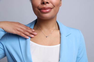 Photo of Young woman wearing elegant silver necklace on light grey background, closeup