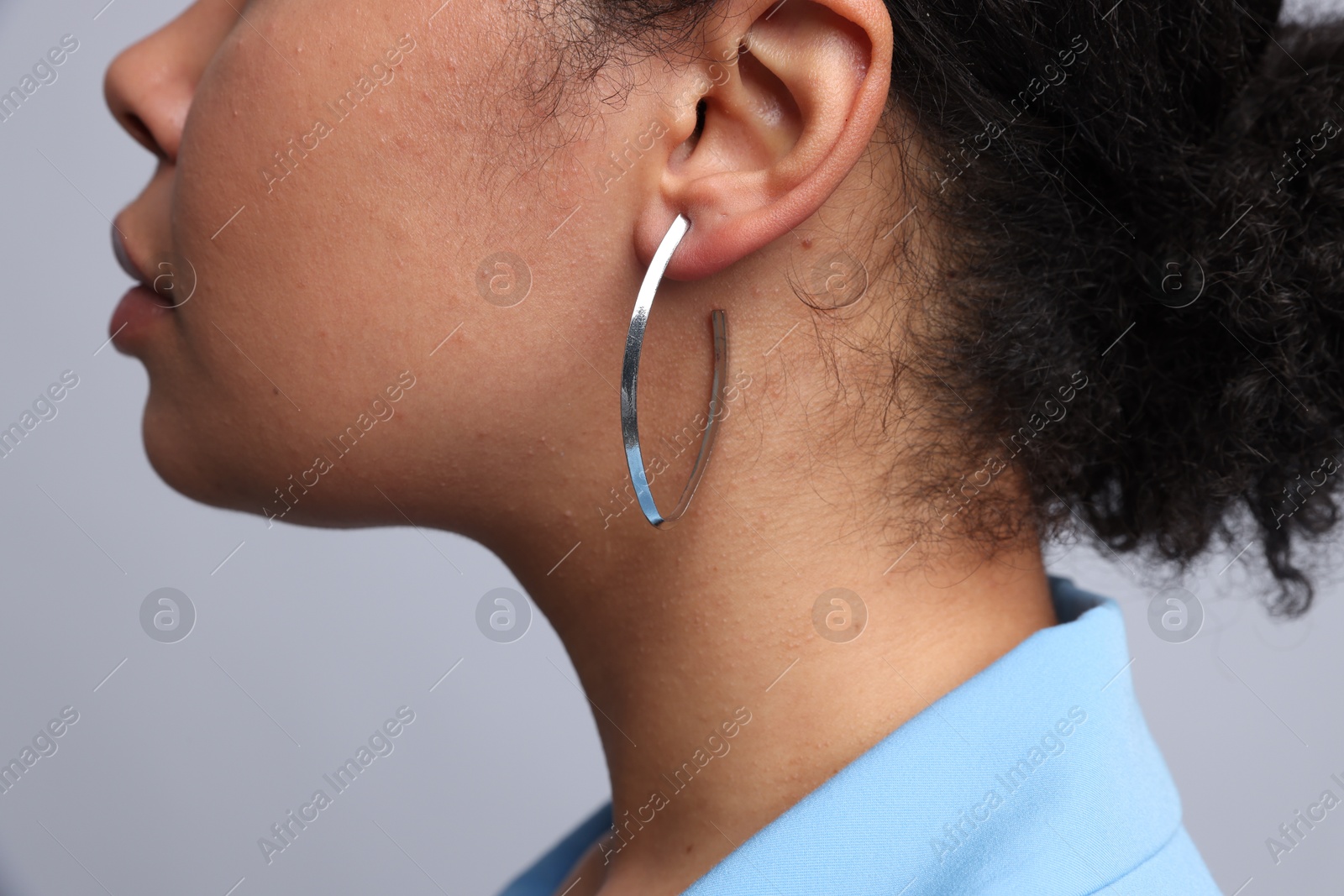 Photo of Young woman wearing elegant silver earring on light grey background, closeup