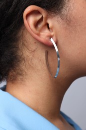 Photo of Young woman wearing elegant silver earring on light grey background, closeup