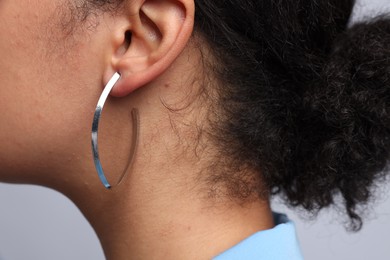 Photo of Young woman wearing elegant silver earring on light grey background, closeup