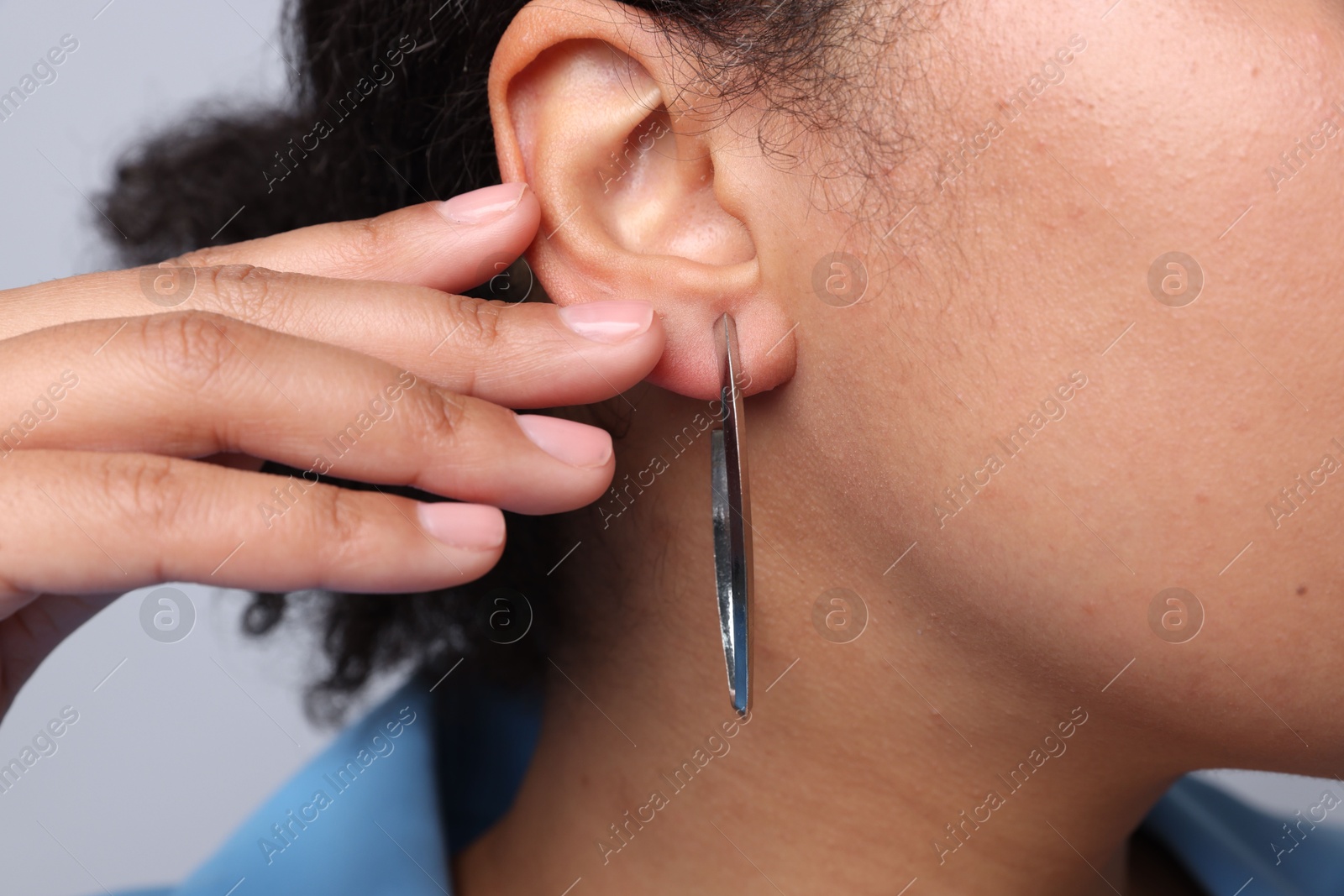 Photo of Young woman wearing elegant silver earring on light grey background, closeup