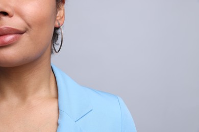 Photo of Young woman wearing elegant silver earring on light grey background, closeup. Space for text