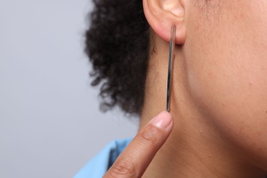 Photo of Young woman wearing elegant silver earring on light grey background, closeup. Space for text