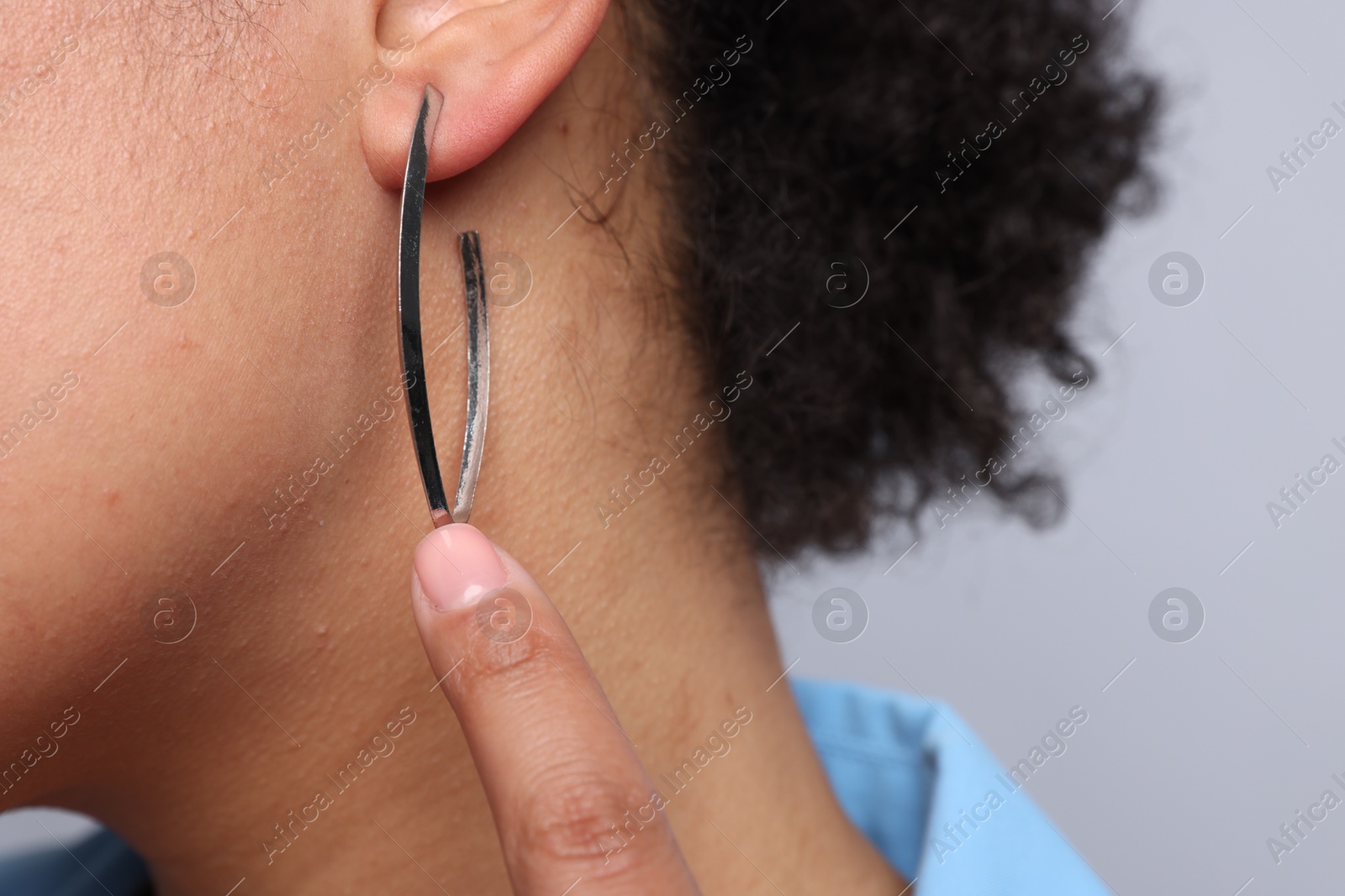 Photo of Young woman wearing elegant silver earring on light grey background, closeup