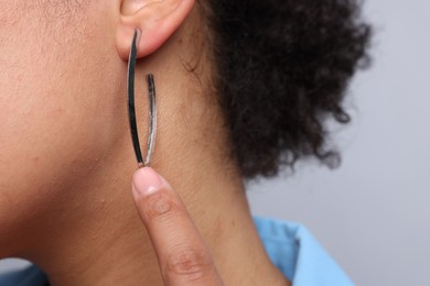 Photo of Young woman wearing elegant silver earring on light grey background, closeup
