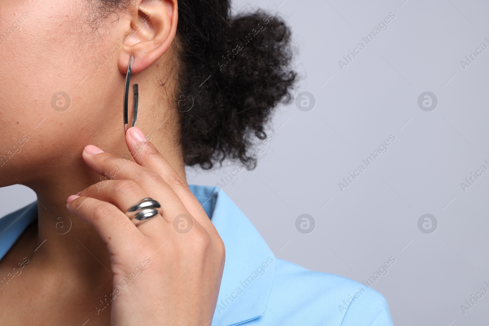 Young woman wearing elegant silver earring and ring on light grey background, closeup. Space for text Photo of Young woman wearing elegant silver earring and ring on light grey background, closeup. Space for text