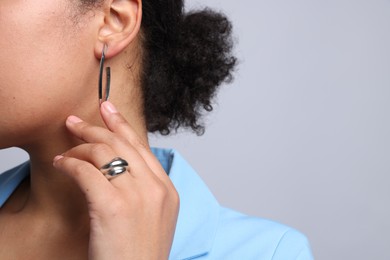 Photo of Young woman wearing elegant silver earring and ring on light grey background, closeup. Space for text