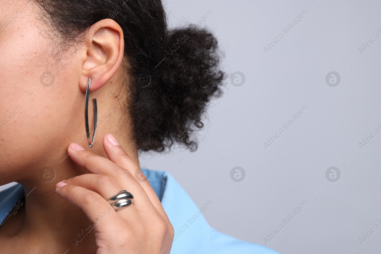 Photo of Young woman wearing elegant silver earring and ring on light grey background, closeup. Space for text