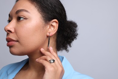 Photo of Young woman wearing elegant silver earring and ring on light grey background. Space for text