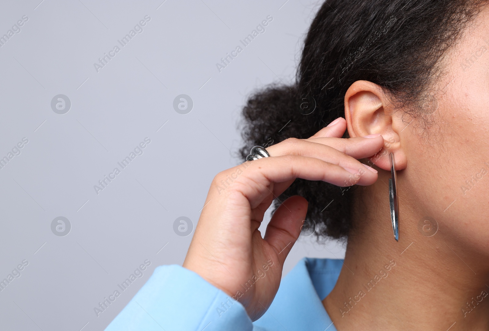 Photo of Young woman wearing elegant silver earring and ring on light grey background, closeup. Space for text
