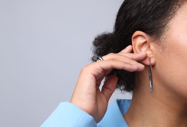 Photo of Young woman wearing elegant silver earring and ring on light grey background, closeup. Space for text