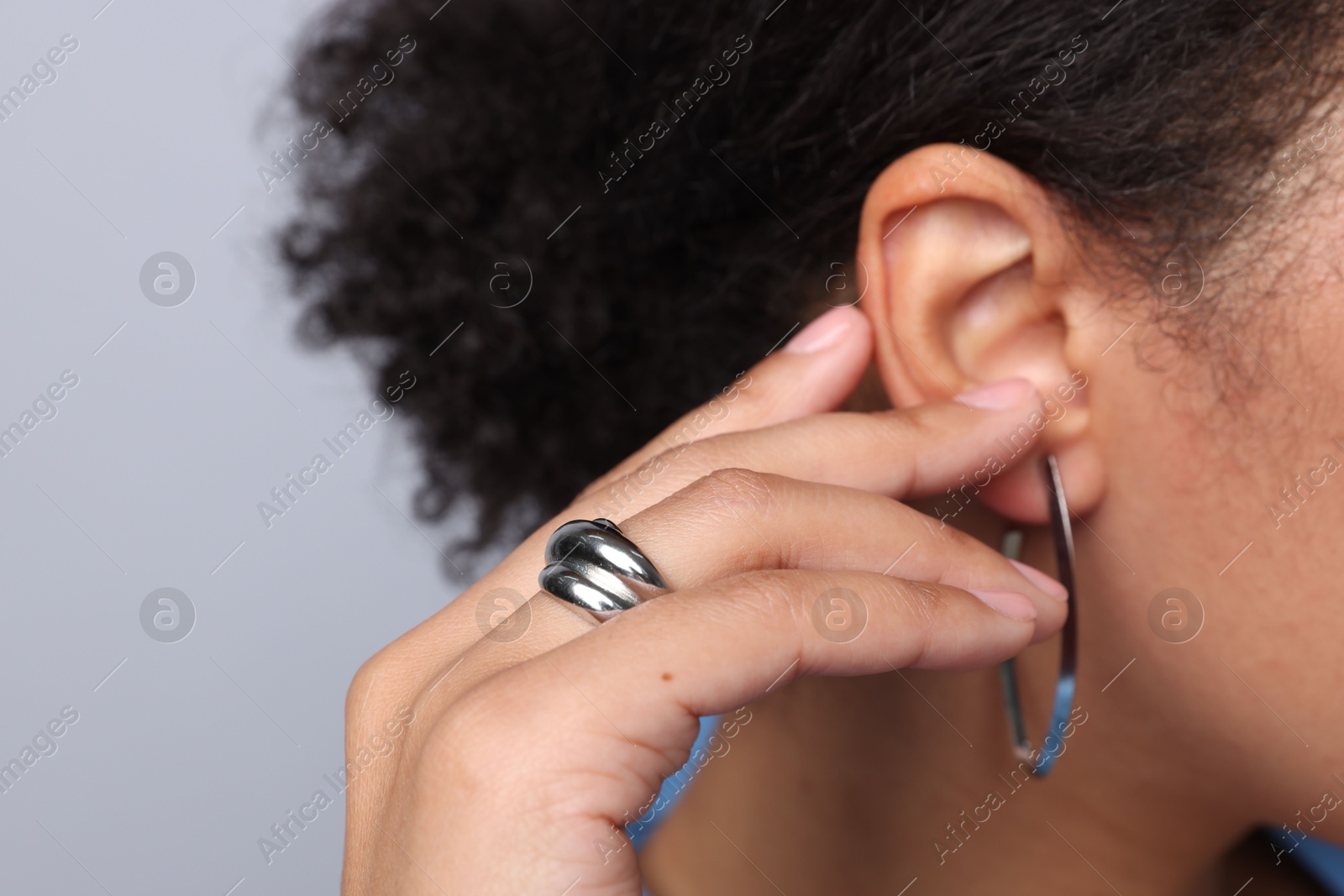 Photo of Young woman wearing elegant silver earring and ring on light grey background, closeup