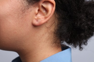 Photo of Young woman with pierced ear on light grey background, closeup