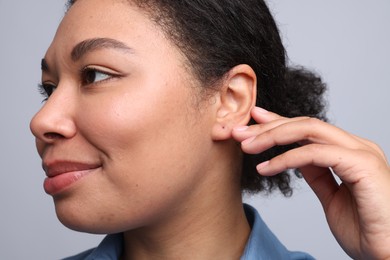 Photo of Young woman with pierced ear on light grey background, closeup