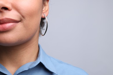 Photo of Young woman wearing elegant silver earring on light grey background, closeup. Space for text