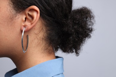 Photo of Young woman wearing elegant silver earring on light grey background, closeup
