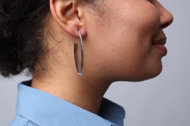 Photo of Young woman wearing elegant silver earring on light grey background, closeup