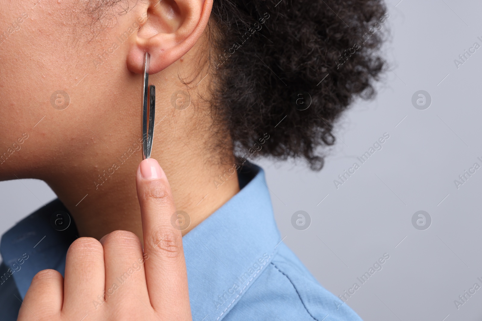 Photo of Young woman wearing elegant silver earring on light grey background, closeup