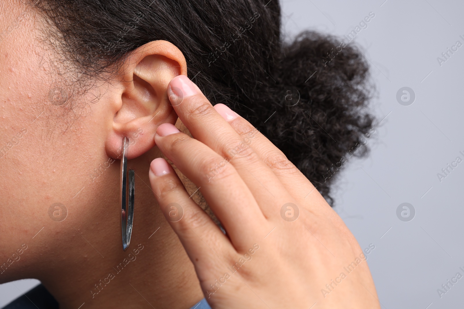Photo of Young woman wearing elegant silver earring on light grey background, closeup